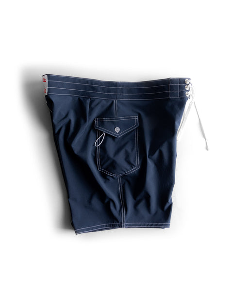 The 808 SurfStretch Side Pocket Boardshorts in navy feature white stitching, a white lace-up waistband, and a flap button back pocket. Made in the USA, they are shown against a white background.