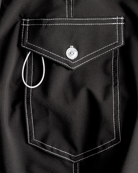 Close-up of the 806 SurfStretch Side Pocket Boardshorts in black, showing white stitching, a silver button closure, and a white wire loop partially tucked into the side pocket.