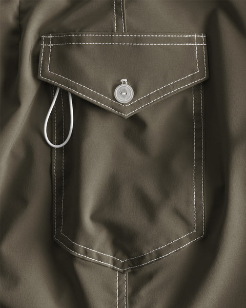 Close-up of the 806 SurfStretch Side Pocket Boardshorts - Army, showing the olive green pocket with white stitching, a flap secured by a silver snap button, and a white cord loop partially tucked under the flap.
