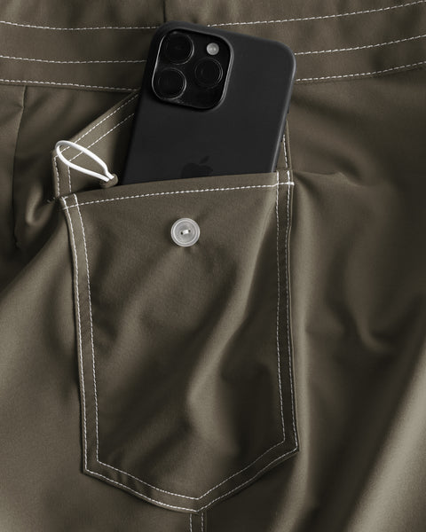 A close-up of the army green side pocket with white stitching on 806 SurfStretch Side Pocket Boardshorts, featuring a button flap, small white loop, and holding a triple-camera black smartphone—crafted for comfort and durability.
