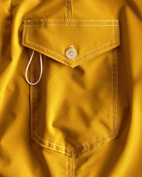 A close-up of the 806 SurfStretch Side Pocket Boardshorts in Gold shows a yellow fabric pocket with white stitching, a flap secured by one button, and a white loop—crafted with the precision of made in the USA boardshorts.