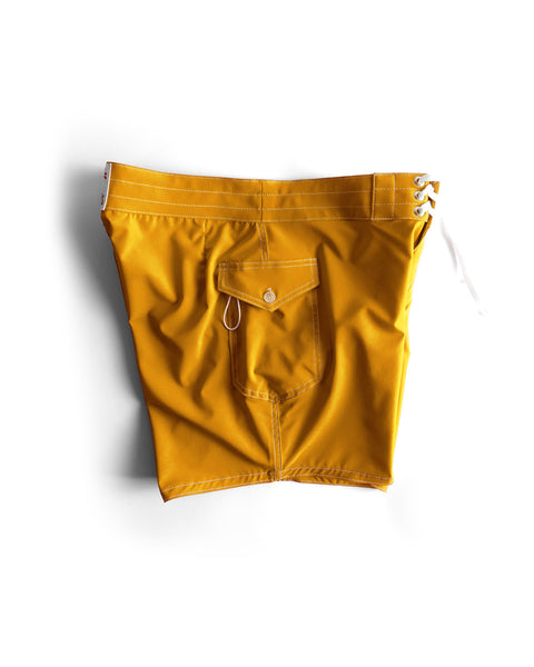 The 806 SurfStretch Side Pocket Boardshorts in gold feature white stitching, a side pocket with button flap and key loop, a white lace-up tie, and are made in the USA. Shown against a white background.