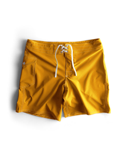 A pair of 808 SurfStretch Side Pocket Boardshorts in gold with a white drawstring, front pocket, and visible stitching are laid flat on a white background.