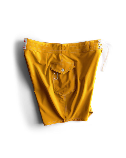 The 808 SurfStretch Side Pocket Boardshorts in Gold feature a bright yellow design, white waist drawstring, red tag accents, and a back buttoned flap pocket, shown against a white background.