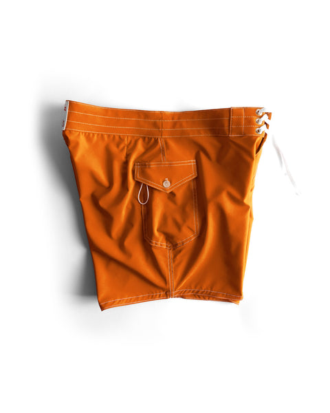 The 806 SurfStretch Side Pocket Boardshorts in medium orange feature white stitching, a back pocket with a button flap, metal key loop, and a white lace-up closure on the right side. Shown laid flat on a white background.