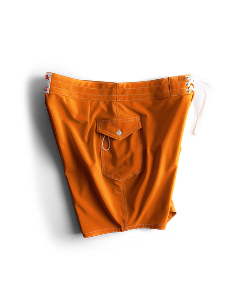 The 808 SurfStretch Side Pocket Boardshorts in medium orange feature white drawstrings, a buttoned back flap pocket, and white stitching. Laid flat on a white background, these stretch boardshorts offer comfort and style.