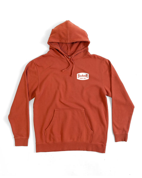 The Herald Midweight Hoodie in Paprika is a relaxed-fit, rust-colored hoodie with a front pocket and a 