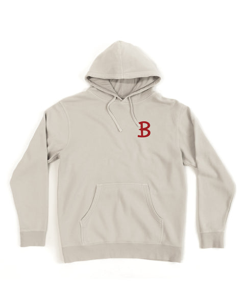 The Script Midweight Hoodie - Bone is a light gray relaxed fit hoodie with a front pocket, drawstrings, and a red letter B screen-print graphic on the left chest.