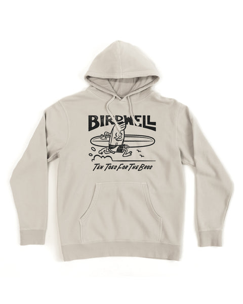 The B-Line Midweight Hoodie - Bone is a light gray relaxed fit hoodie with a cartoon surfer and surfboard graphic, “BIRDWELL” above, and “Ten Toes For The Bros” below, displayed flat on a white background.