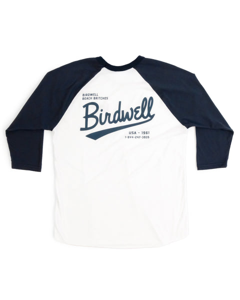 The Baller 3/4 Sleeve Raglan - White/Navy features a garment-dyed white body, navy raglan sleeves, large scripted Birdwell text on the back, Beach Britches USA - 1961 details, and a phone number.