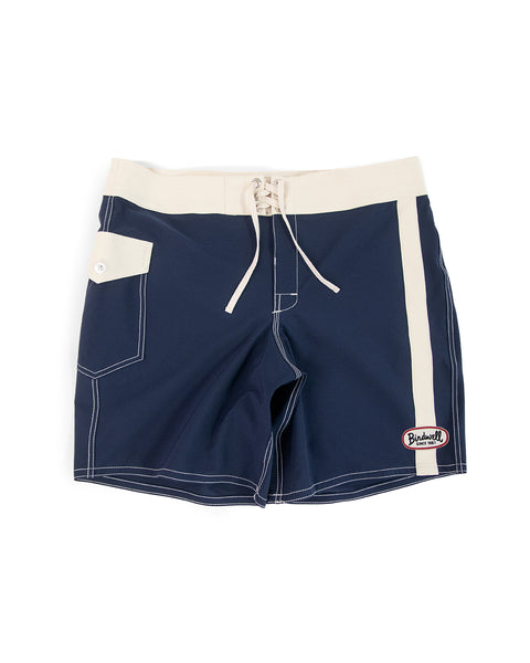 The 808 Mono Stripe - Navy/Bone boardshorts feature a classic navy design with bone waistband, drawstring, and side stripe, plus a side pocket with button flap and Budweiser patch on the front left leg. Made in the USA.