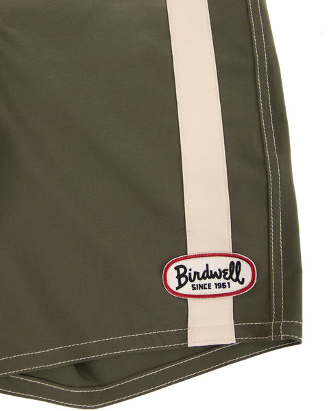 Close-up of the 808 Mono Stripe boardshorts in Army/Bone, featuring a beige vertical stripe and a Birdwell patch near the hem. Proudly made in the USA.