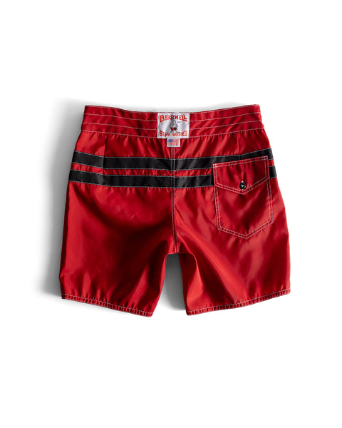 The 300 Comp Stripe - Red/Black boardshorts feature black stripes across the back, a right buttoned back pocket, and a white waistband label with red and blue text. Made in the USA, these classic trunks are shown flat on a white background.