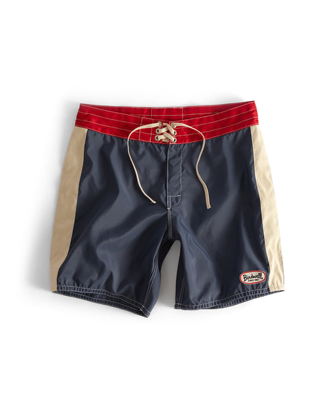 The 300 Legend - Navy/Red/Bone men’s boardshorts feature a red waistband, beige side panels, dark blue front and back, lace-up front, small embroidered patch on the lower left leg, and are made in the USA.