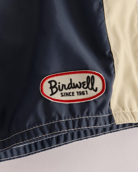Close-up of the 300 Legend - Navy/Red/Bone, showing navy and cream SurfNyl fabric with white stitching and an oval Birdwell SINCE 1961 patch, highlighting classic boardshorts proudly made in the USA.
