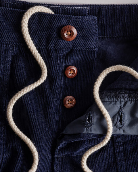 Close-up of Classic Corduroy Shorts - Navy, showing an adjustable waist with three brown buttons and a cream drawstring, partially open to reveal gray inner lining and buttonholes.