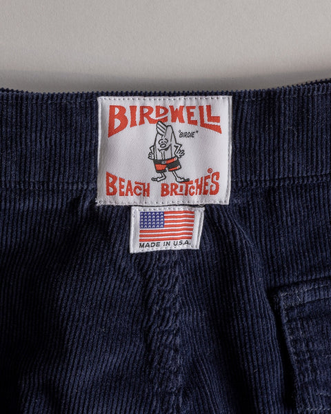 Close-up of Classic Corduroy Shorts - Navy waistband, showing a Birdwell label with cartoon bird, adjustable drawcord waist, and a separate “MADE IN U.S.A.” tag with small American flag below.