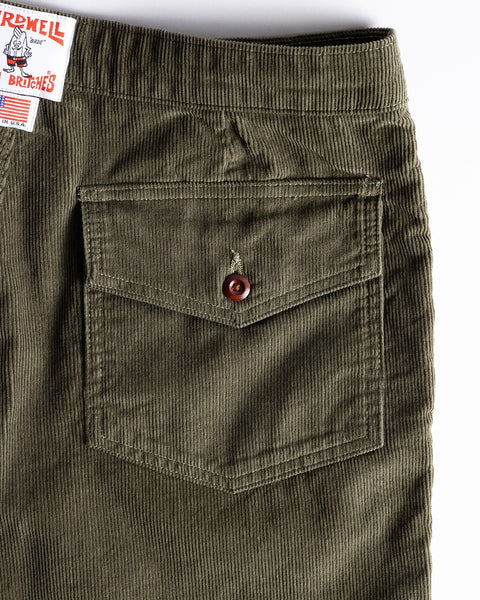 Close-up of the back pocket on Classic Corduroy Shorts - Olive, featuring a flap with brown button closure and a partial label visible in the upper left corner.