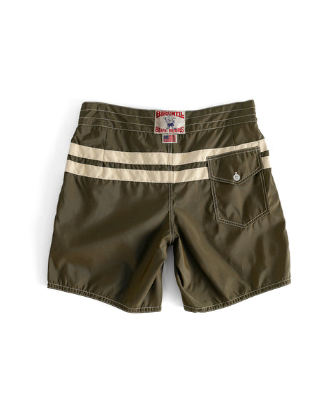 The 300 Comp Stripe boardshorts in Dark Olive/Bone feature a beige back stripe, single buttoned flap pocket, and red label above the waistband. Made in the USA and shown laid flat on a white background.