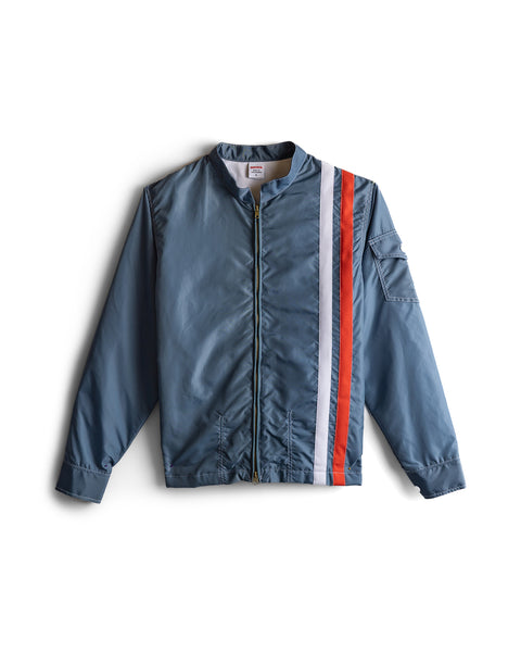 The Racing Jacket 26 in Federal Blue features a front zipper, two vertical stripes—white and orange—down the left side, a left sleeve pocket, plus ribbed cuffs and hem for classic American-made style.