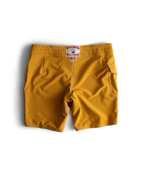 A pair of 808 Racing Stripes swim trunks in gold and bone with white stitching and a back pocket, displayed flat on a white background. The waistband features a BIRDWELL BEACH BRITCHES label. Made in the USA.