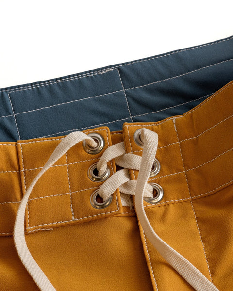 Close-up of the waistband of 808 Racing Stripes - Gold/Bone SurfStretch® swim trunks featuring white stitching, silver eyelets, a white drawstring laced through the front, and a blue interior waistband with premium comfort.