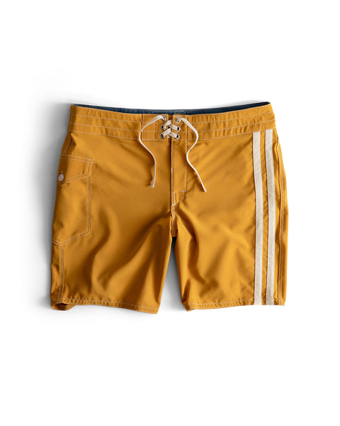 808 Racing Stripes swim trunks in Gold/Bone, featuring a drawstring waist, white side stripes, and a front pocket, shown flat on a white background.