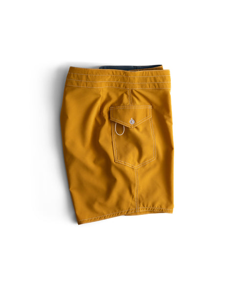 A folded pair of 808 Racing Stripes shorts in Gold/Bone, featuring a back pocket with buttoned flap and small hoop detail, is displayed on a white background. These comfortable SurfStretch® boardshorts are made in the USA.