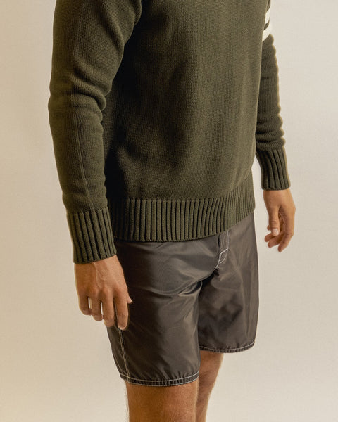A person wearing a dark green knit sweater and brown 310 Boardshorts stands against a plain light background, with only the lower torso and arms visible.