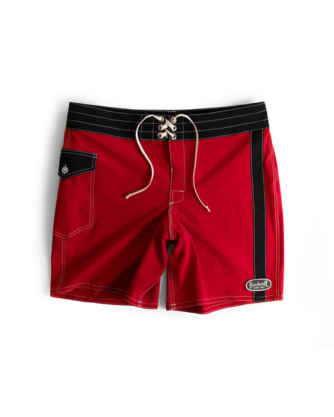 The 808 Mono Stripe - Red/Black are red SurfStretch boardshorts with white stitching, black waistband and side stripe, front lace-up closure, small black flap pocket, and Birdwell logo patch. Made in the USA.
