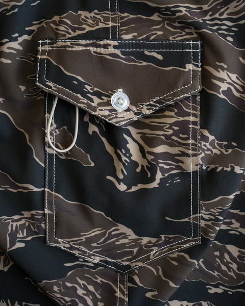 Close-up of the 808 SurfStretch Side Pocket Boardshorts - Tiger Camo, showing a buttoned flap pocket with brown, black, and beige camo pattern, white stitching, and quality detailing that highlights its made in the USA craftsmanship.