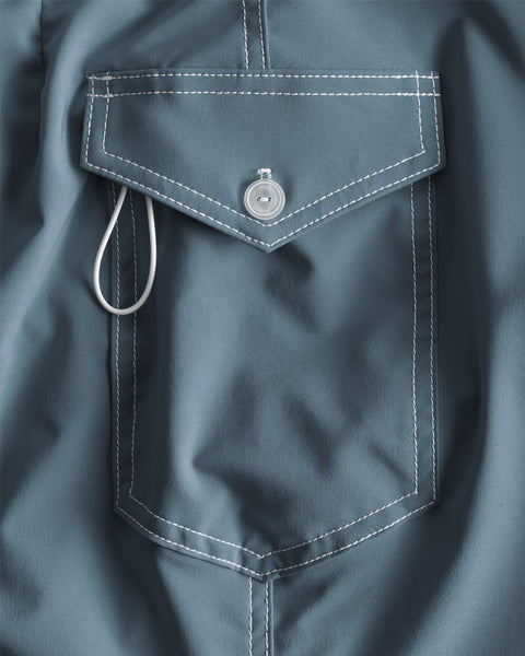 A close-up of the 808 SurfStretch Side Pocket Boardshorts in Federal Blue shows the pocket's white stitching, button closure, and a white cord loop partly under the flap. This medium-length boardshort is proudly made in the USA.