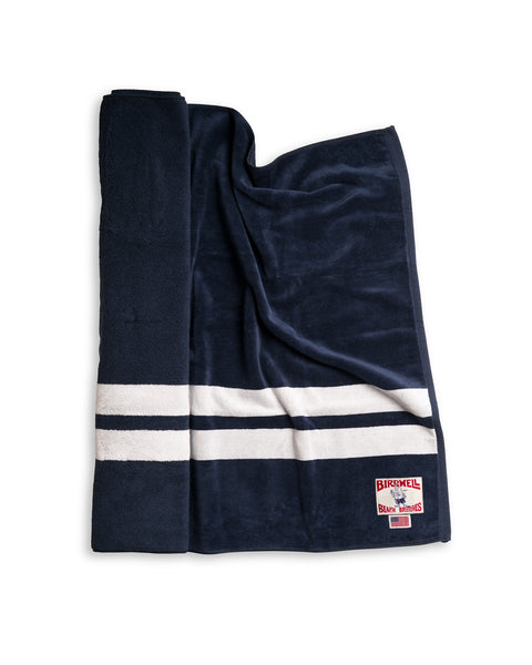 The Comp Stripe Towel - Navy/White is an oversized 100% cotton towel made in the USA, featuring two white horizontal stripes and a Birkmel Blank Brothers patch on navy fabric, shown against a white background.