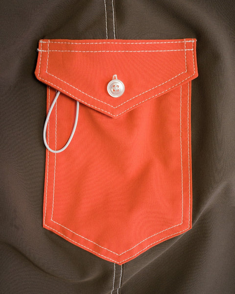 The 808 Pop Pocket - Brown/Paprika features an orange fabric pocket with white stitching and a button closure sewn onto a brown background, plus a white cord detail inspired by USA-made SurfStretch boardshorts.