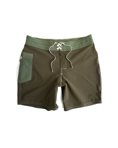 The 808 Pop Pocket boardshorts in Dark Olive/Olive feature a lighter green waistband, white drawstring, left side pocket, SurfStretch fabric, white stitching, and are made in the USA. Shown laid flat on a white background.