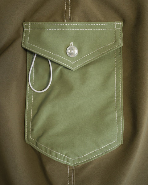 A close-up of the 808 Pop Pocket in Dark Olive/Olive shows a pocket with white stitching and a buttoned flap made from SurfStretch fabric. A white cord or wire is partially tucked in, with its loop showing outside.