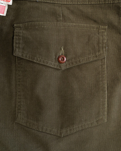 Close-up of a pocket on the Classic Corduroy Pants - Dark Olive, featuring olive green corduroy fabric, a flap secured by a brown button, and details that capture their timeless style. A glimpse of a red and white clothing tag appears in the top left corner, subtly indicating these pants are proudly made in Southern California.