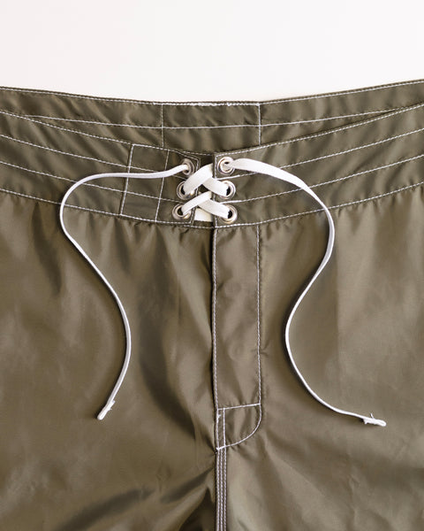 Close-up of the waistband of the 312 Boardshorts in Dark Olive, highlighting white stitching and white lace-up drawstrings threaded through metal eyelets in a crisscross pattern at the front. These long-length boardshorts are proudly made in the USA for exceptional quality and durability.