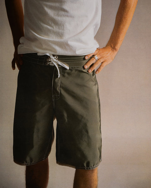 A person wearing a white t-shirt and 312 Boardshorts - Dark Olive stands with hands on hips against a plain background.