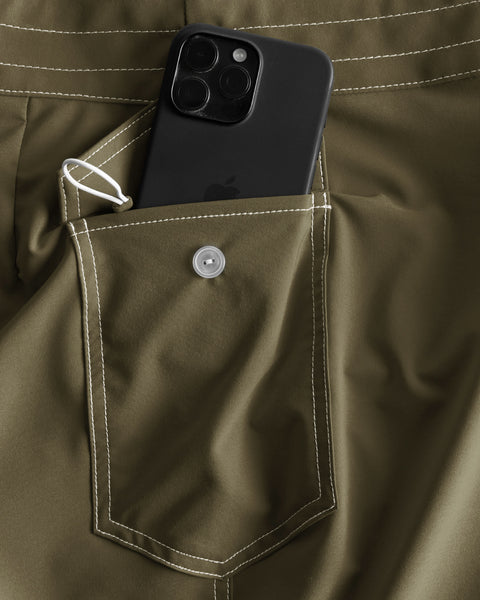 A black smartphone partially sticks out of the side pocket on the 806 SurfStretch Side Pocket Boardshorts in Dark Olive, highlighting their innovative SurfStretch fabric and distinctive white stitching. Proudly made in the USA.