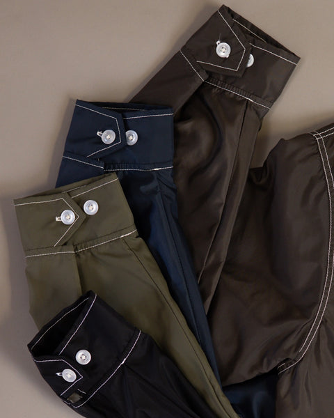 Three long sleeve cuffs from the Racing Jacket 26 - Dark Olive/Bone/Black, featuring vintage-inspired design with white contrast stitching and buttons, laid flat on a beige background.