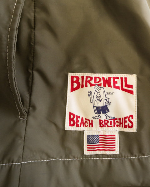 A patch on khaki fabric reads Birdwell Beach Britches, featuring a cartoon character and an American flag below—details that reflect the American-made heritage of the Racing Jacket 26 - Dark Olive/Bone/Black.