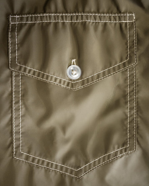 Close-up of a dark olive fabric pocket with white stitching and a single button closure at the top center. The material appears to be from the Racing Jacket 26 - Dark Olive/Bone/Black, crafted in Birdwell’s signature durable SurfNyl fabric, often seen on classic jackets or shirts.