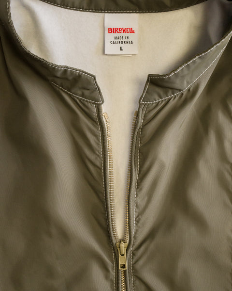 Close-up of the Racing Jacket 26 in Dark Olive/Bone/Black, featuring a beige lining, white stitching, and a visible zipper. Crafted from durable SurfNyl fabric, the label reads BIRDWELL MADE IN CALIFORNIA L.