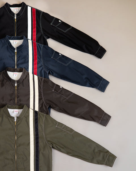 Four Racing Jacket 26 - Dark Olive/Bone/Black styles are laid out diagonally, each with a vertical left stripe and a sleeve pocket with flap. Available in black, navy, brown, and olive.