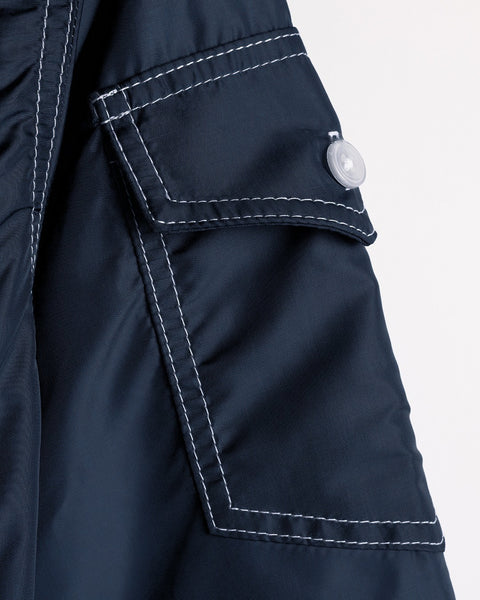 Close-up of a navy blue SurfNyl fabric pocket with white stitching and a flap secured by a translucent button on the American-made Racing Jacket 26 - Navy/Bone/Red garment.