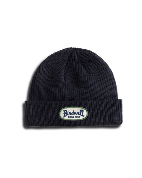 A navy fisherman-style beanie with a cuffed hem and folded brim, featuring a white oval patch that reads Birdwell Since 1961. The Potato Watchcap is photographed on a white background.