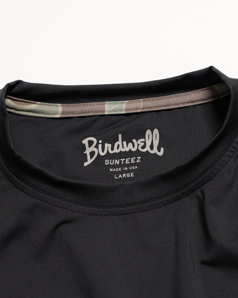 Close-up of the collar on the Sunteez Short Sleeve - Black, featuring the Birdwell Sunteez Made in USA Large print inside. A camouflage lining accents the inside of the collar, showcasing this UPF50+ shirt’s precise craftsmanship and superior sun protection.