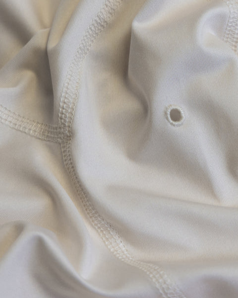 Close-up of the Sunteez Long Sleeve - Bone featuring white performance stretch fabric with visible stitching, a small hole, and gentle folds that create soft shadows and textured detail.
