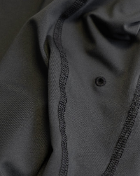 Close-up of black fabric with visible stitching and a small grommet or hole, highlighting the texture and details of the material—this Sunteez Short Sleeve - Black shirt offers moisture-wicking comfort and UPF50+ protection for superior wearability.